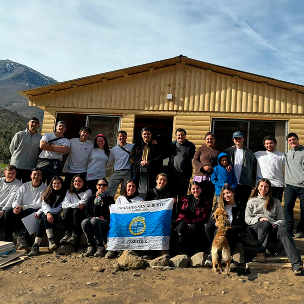 Un grupo de hombres y mujeres con una bandera frente a una casa de madera