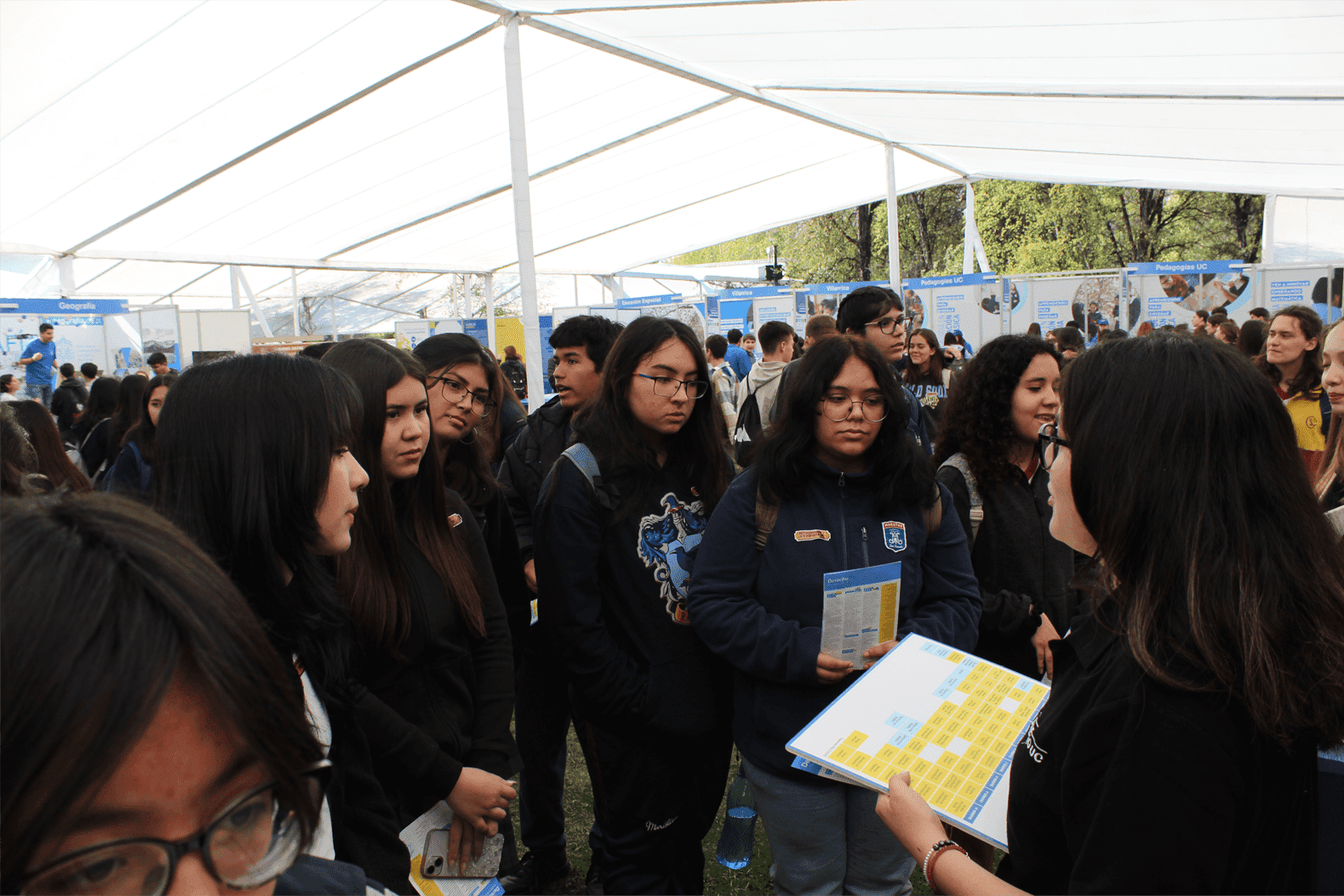 Un grupo de estudiantes escuchando a una persona en una feria estudiantil al aire libre