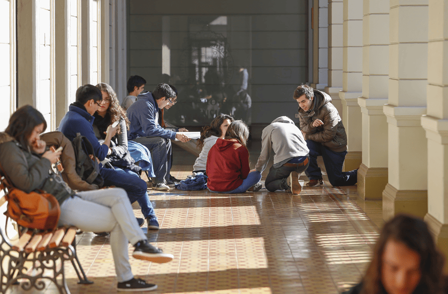 Estudiantes sentados en bancas y en el suelo en un pasillo