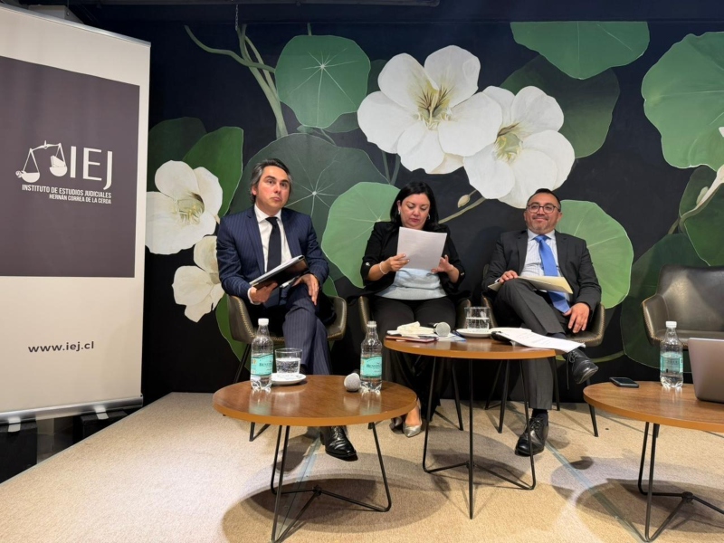 Participantes en una conferencia del Instituto de Estudios Judiciales, leyendo documentos. Con fondo llamativo de flores.