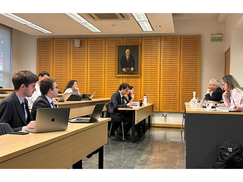 estudiantes en una reunión académica en una sala con un retrato en la pared